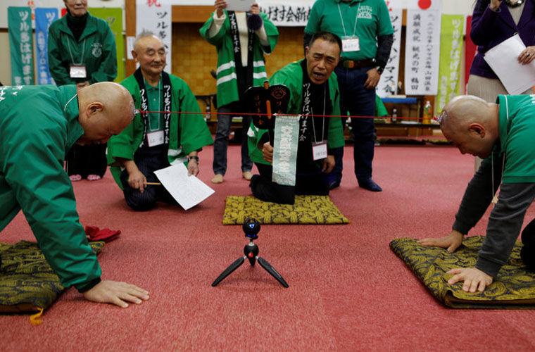 Members of the Bald Men Club, take part in a unique game of tug-of-war by attaching suction pads onto their heads, at a hot spring facility in Tsuruta town by STAFF. 